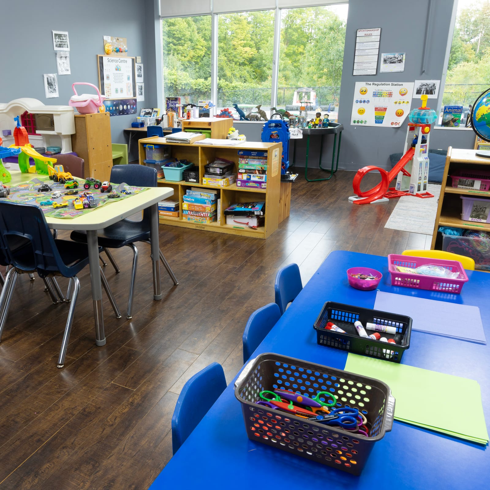 A bright Tender Years classroom with activity tables, low shelves and large windows looking out on trees