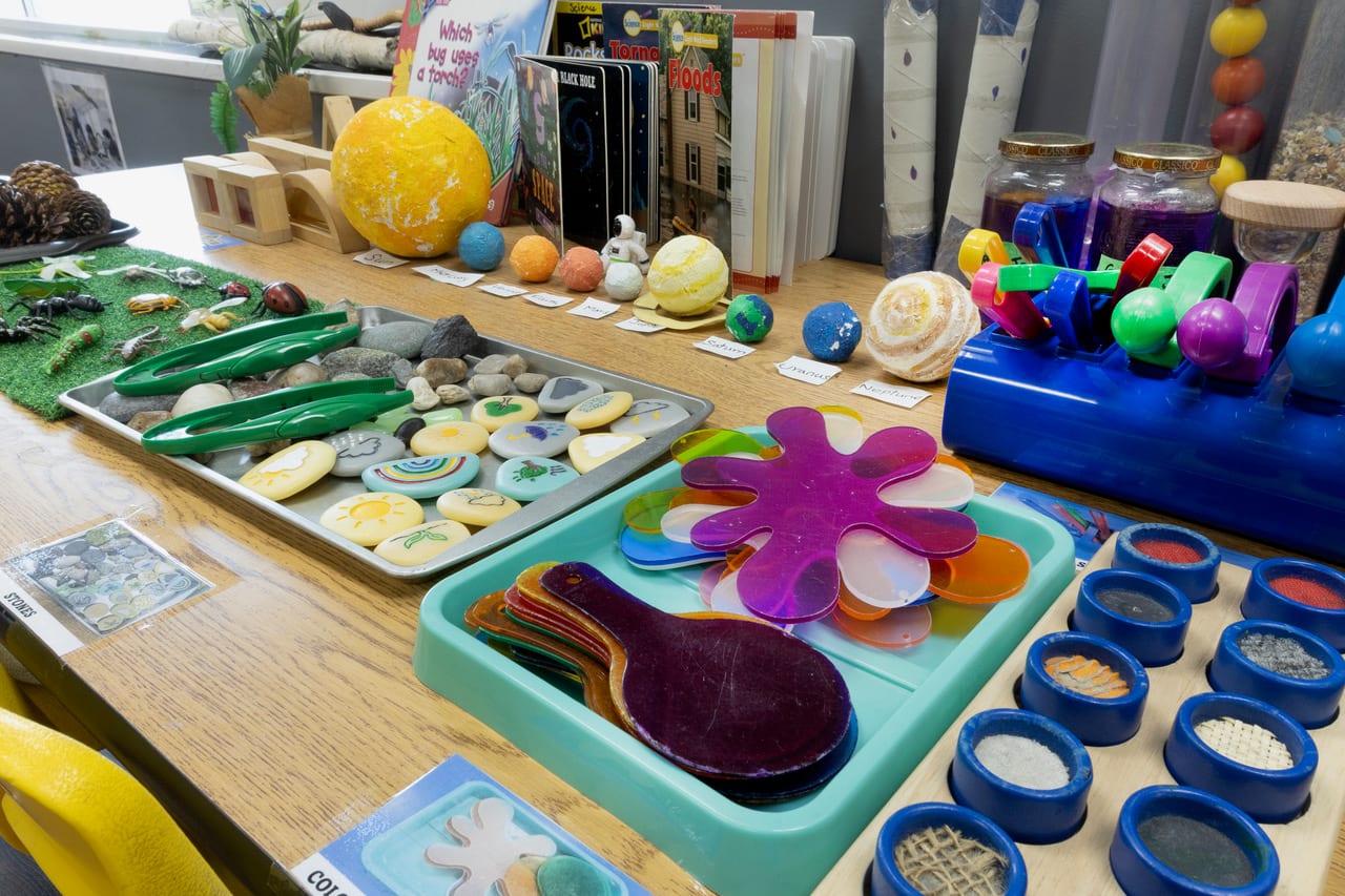 A science and discovery table with painted stones, colour paddles and sensory tubs