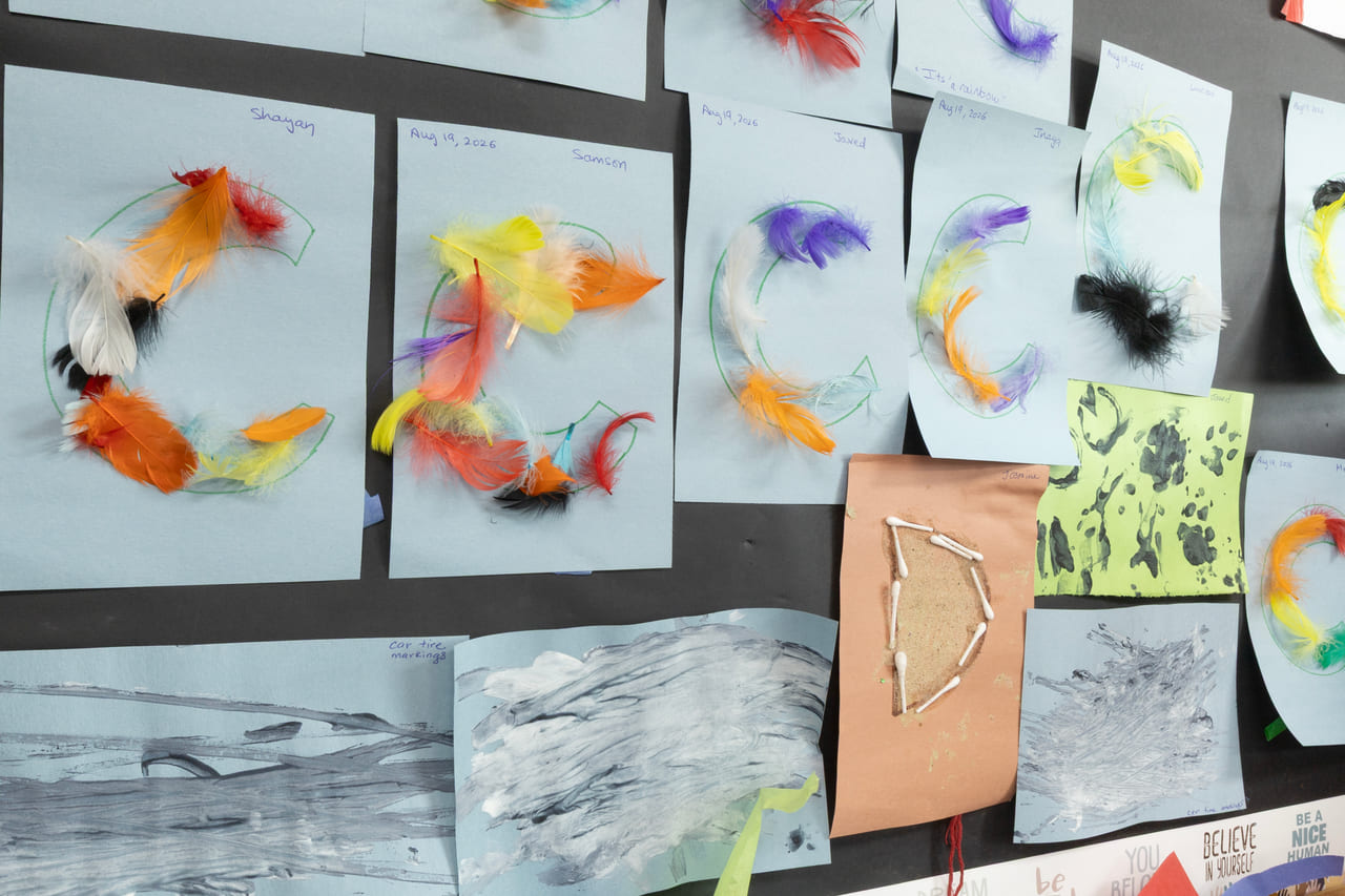 Children's feather and paint artwork displayed on the classroom wall