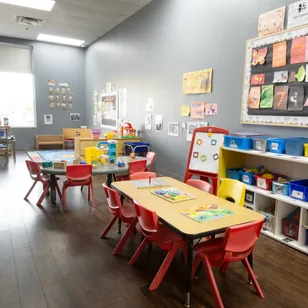 A bright preschool room with red chairs, activity tables and children's artwork