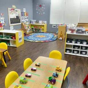 A wide classroom with child-size tables, an alphabet rug and low toy shelves