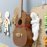 A ukulele beside children's pom-pom and cotton collage artwork
