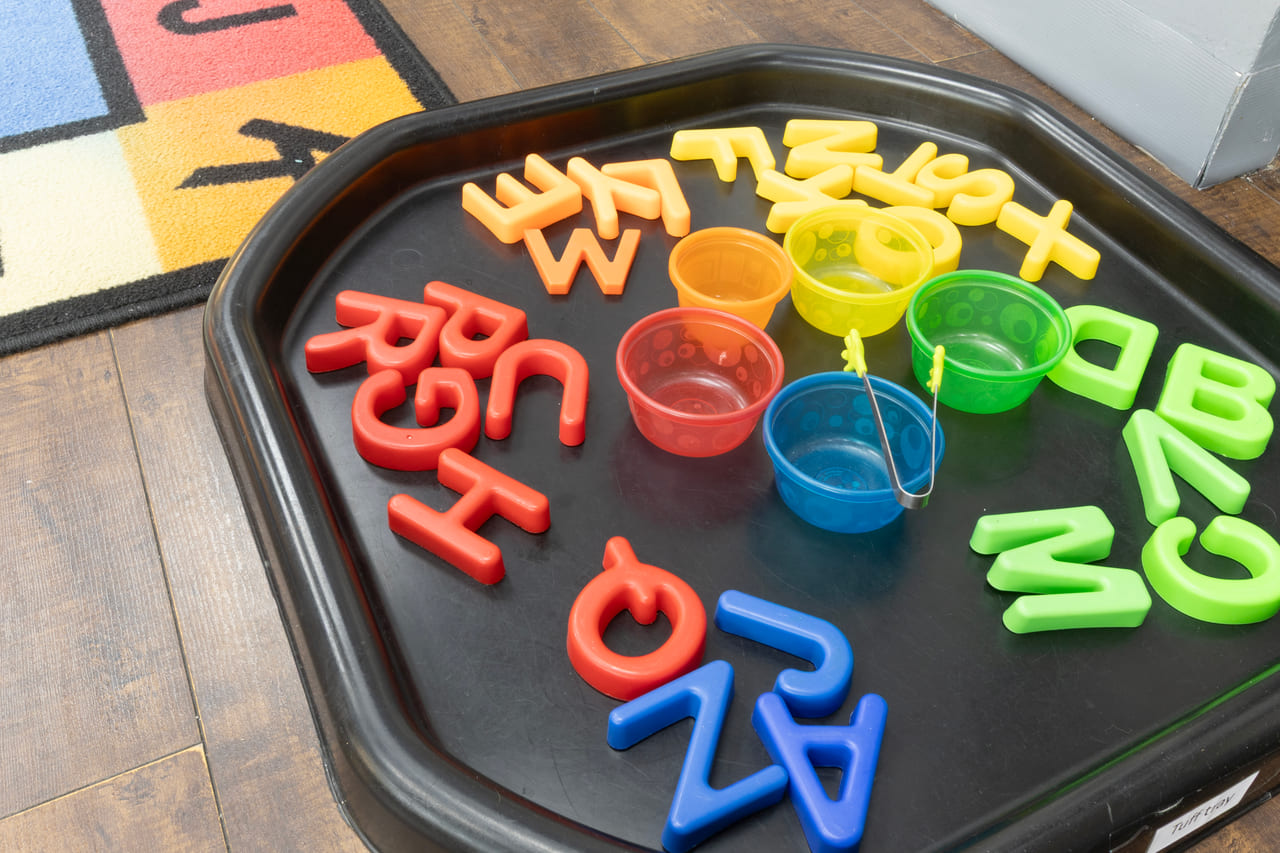 Foam letters, scoops and bowls arranged in a black tuff tray