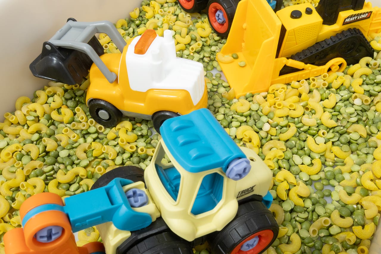 A sensory bin of dry pasta with toy diggers and trucks
