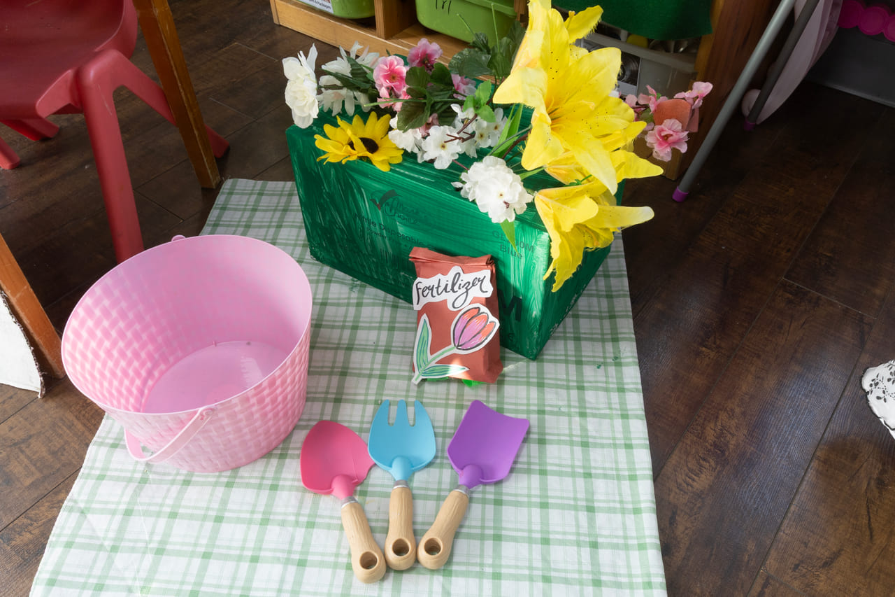 A flower-shop play table with a planter of daffodils, a watering basket and wooden scoops