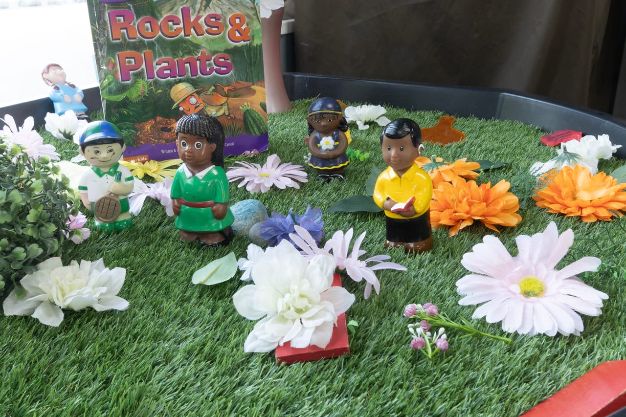 A small-world play tray with artificial grass, flowers, rocks and toy figures