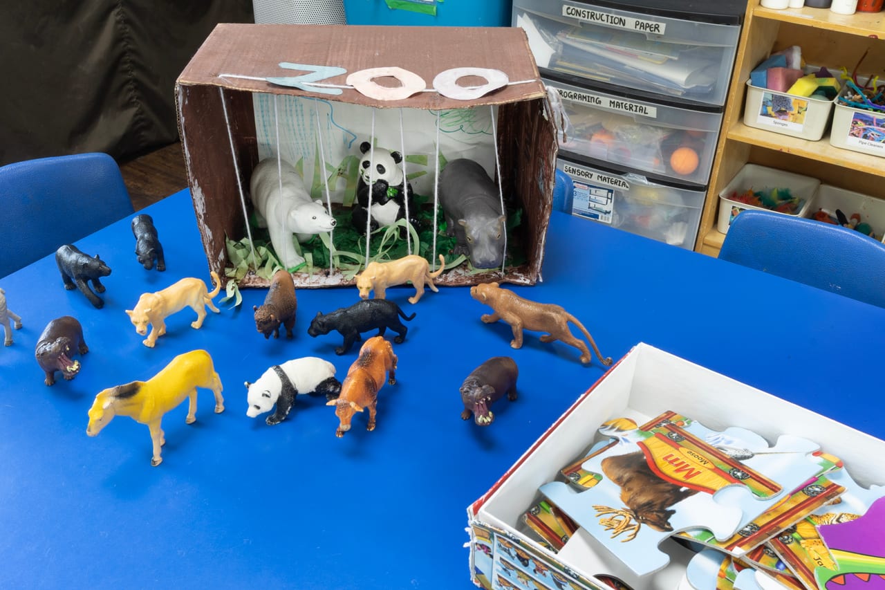 A zoo play scene with toy animals and a cardboard enclosure