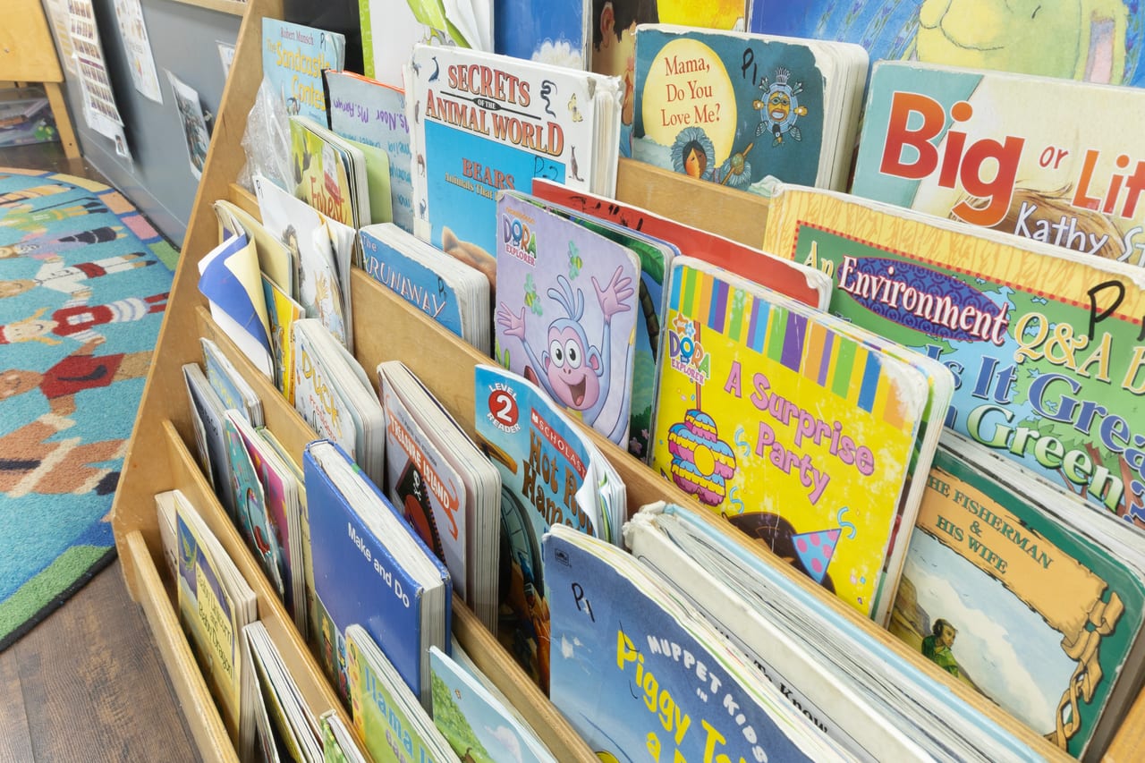 A rack filled with picture books beside the classroom carpet