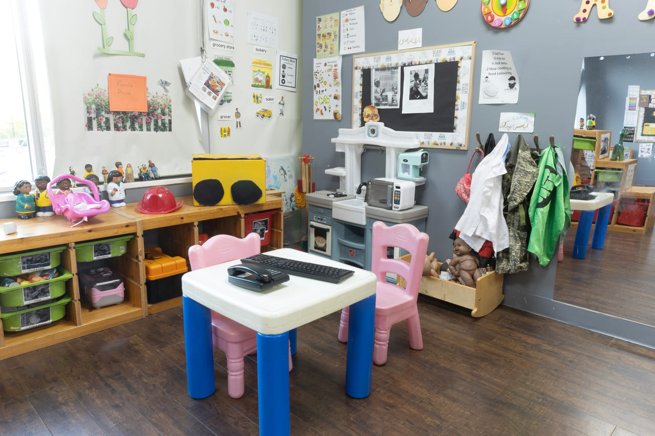 A wide preschool room with a play kitchen, dress-up corner and open shelving