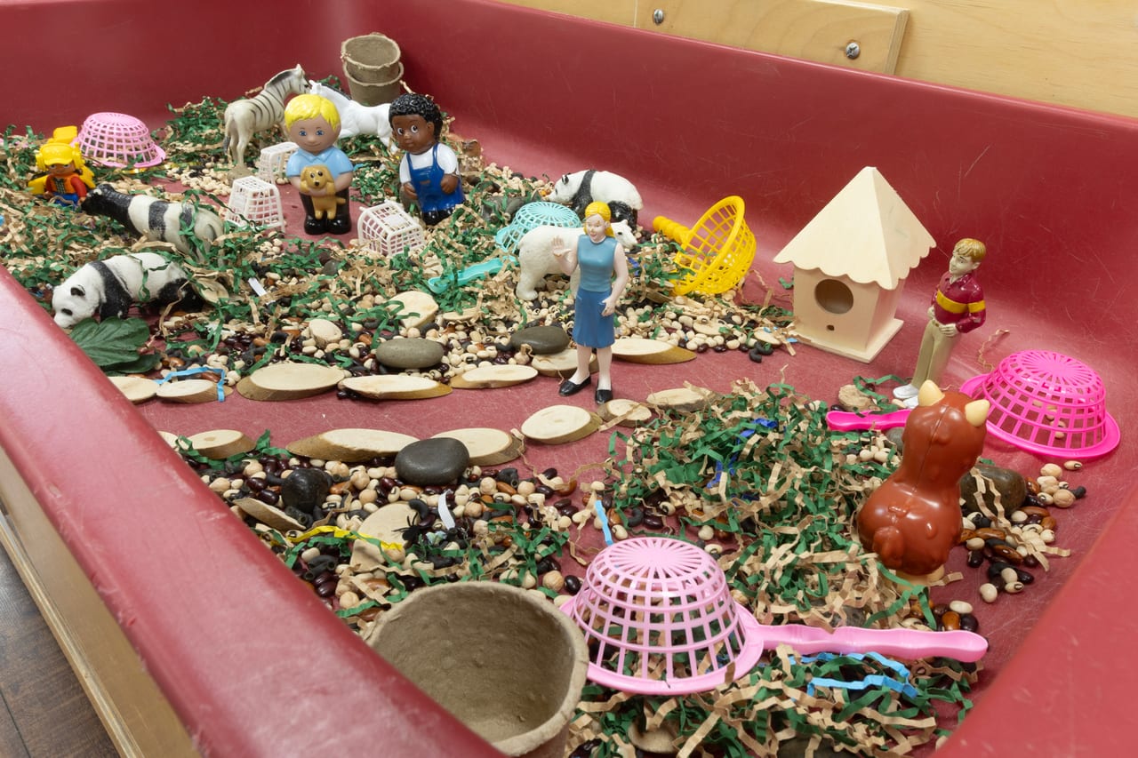 A small-world sensory bin with figures, animals, stepping stones and scoops