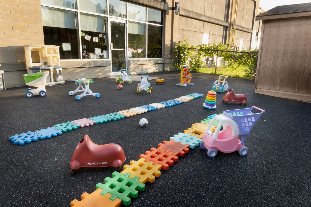 The enclosed toddler yard at Tender Years, with ride-on toys and a foam play path
